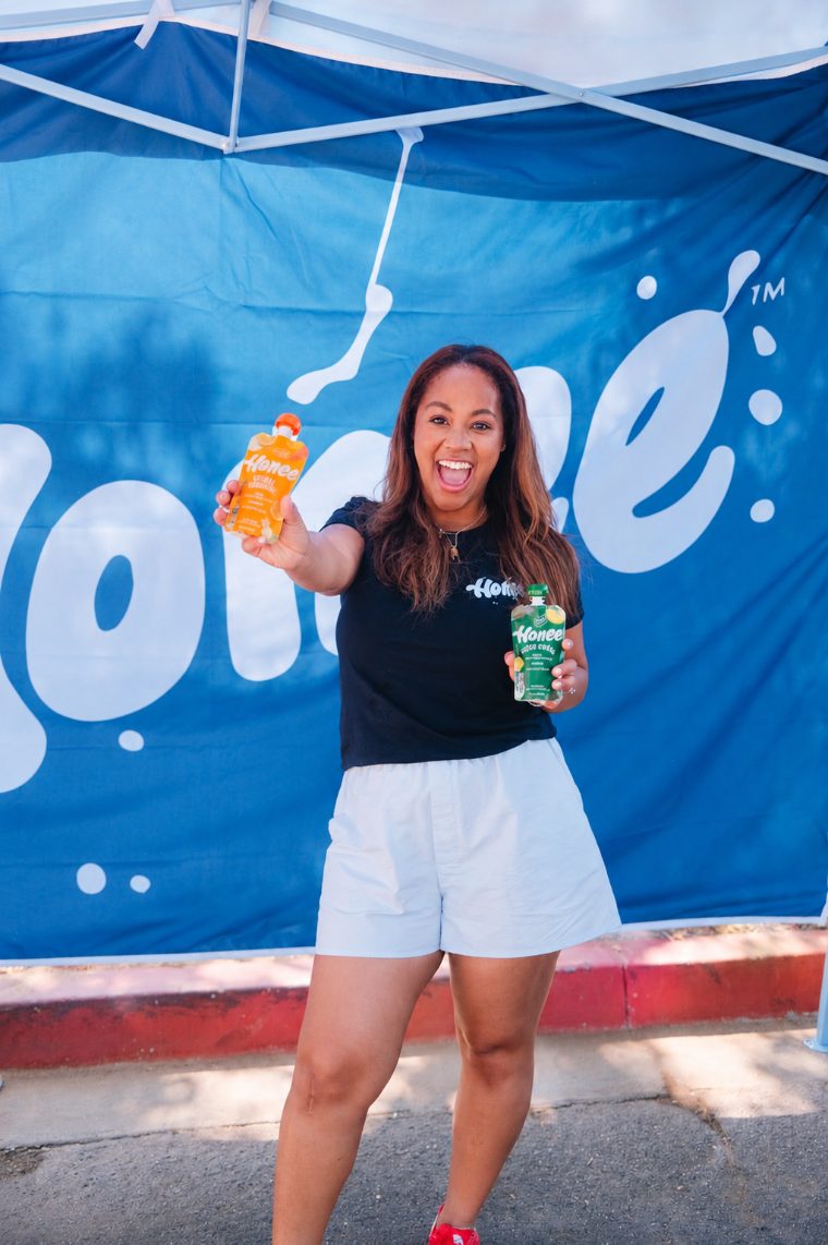 Honee founder holding up two pouches in front of the Honee banner