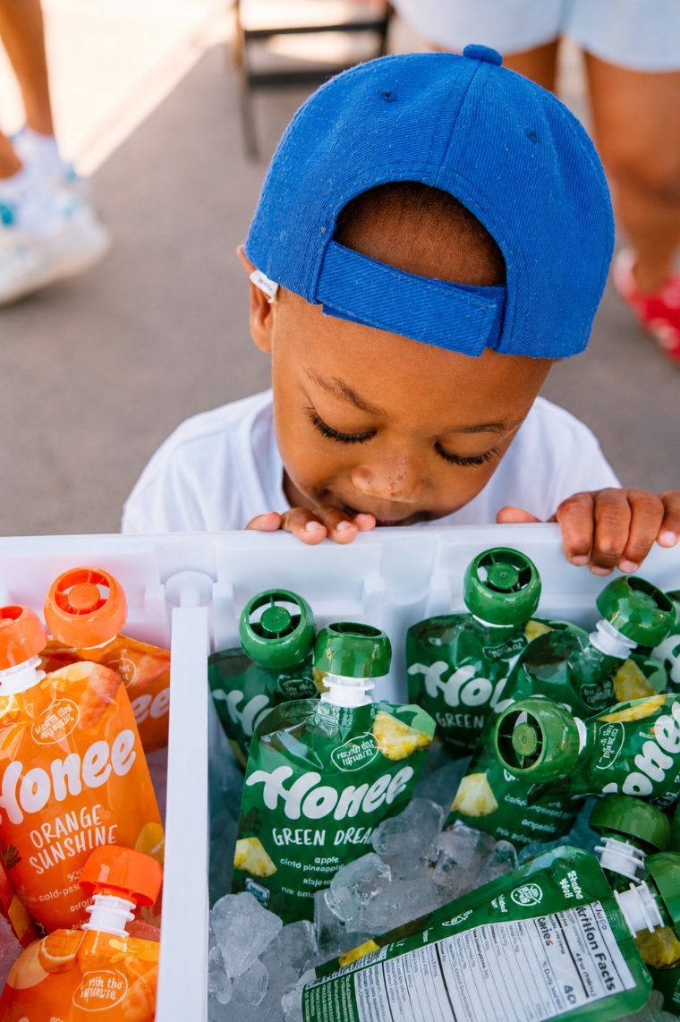 A toddler leaning over a cooler filled with iced Honee pouches