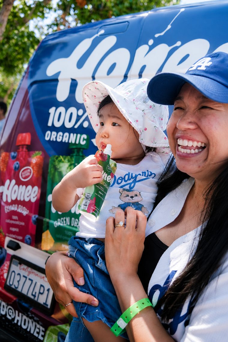 A mother and baby enjoying a Honee pouch beside the branded van