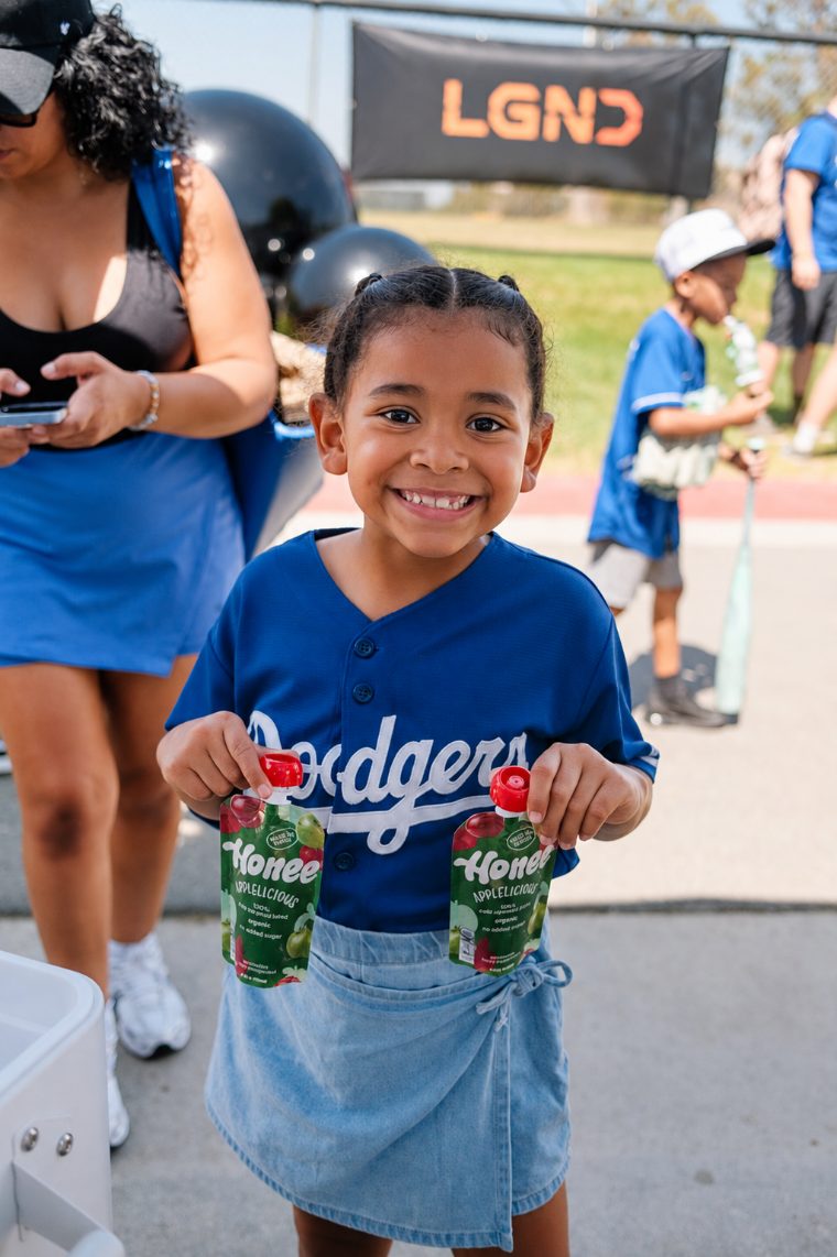 A girl in a Dodgers jersey holding two Applelicious pouches